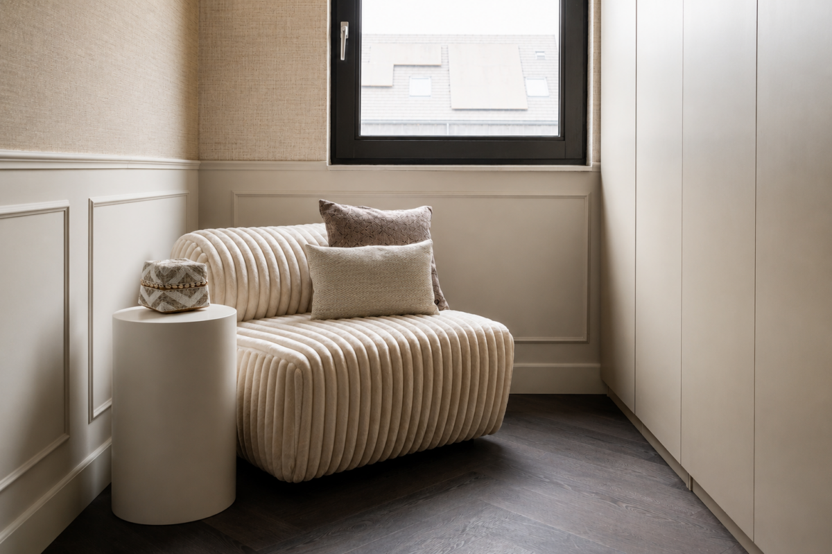 Rustige loungehoek in slaapkamer met zachte fauteuil, sierkussens en natuurlijke materialen.